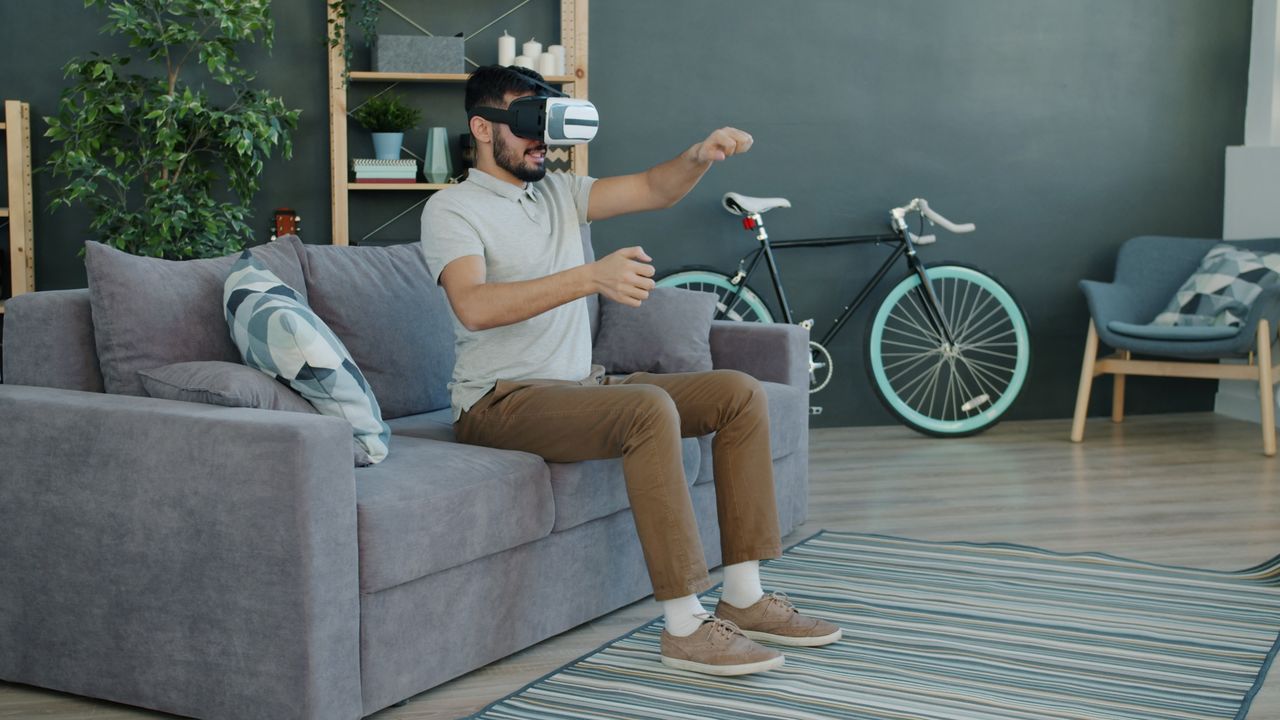 A man wearing a VR headset experiences virtual reality while seated on a sofa in a contemporary living room.